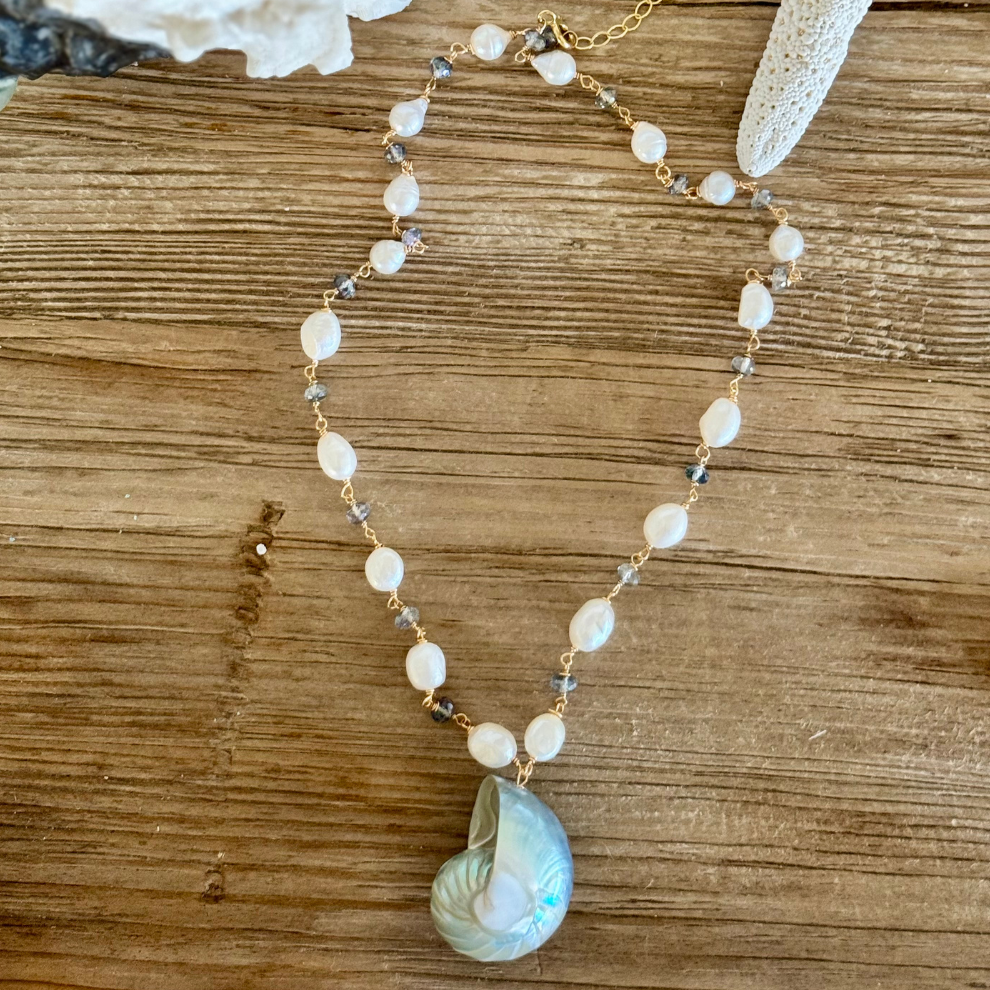 Genuine blue nautilus shell pendant on beachy wood surface. Freshwater pearls and mystic topaz accents between 14k gold-filled wire and chain. Displayed between starfish and coral.