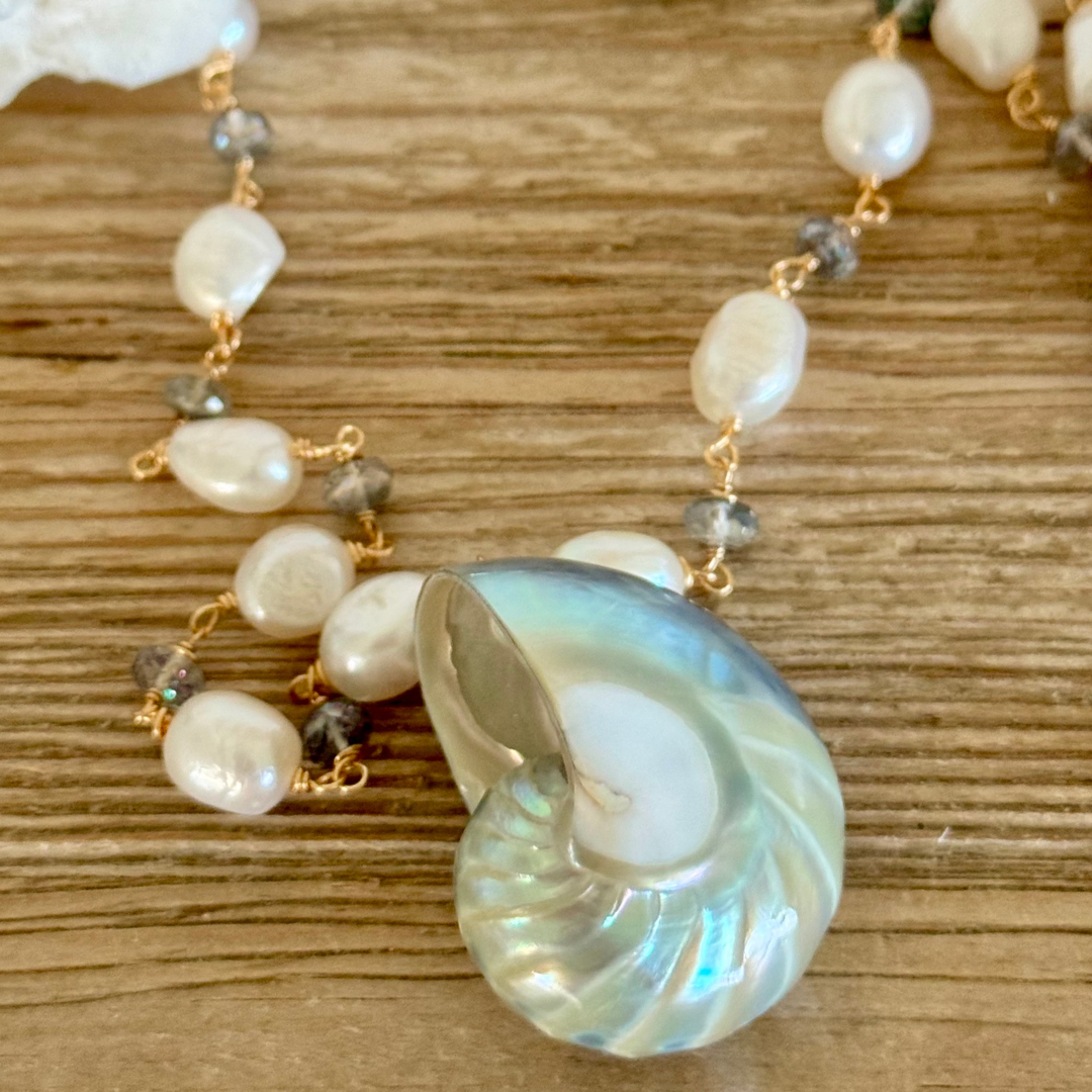 Up close image of genuine blue nautilus shell pendant necklace with freshwater pearls and mystic topaz accents on 14k gold-filled wire and chain.