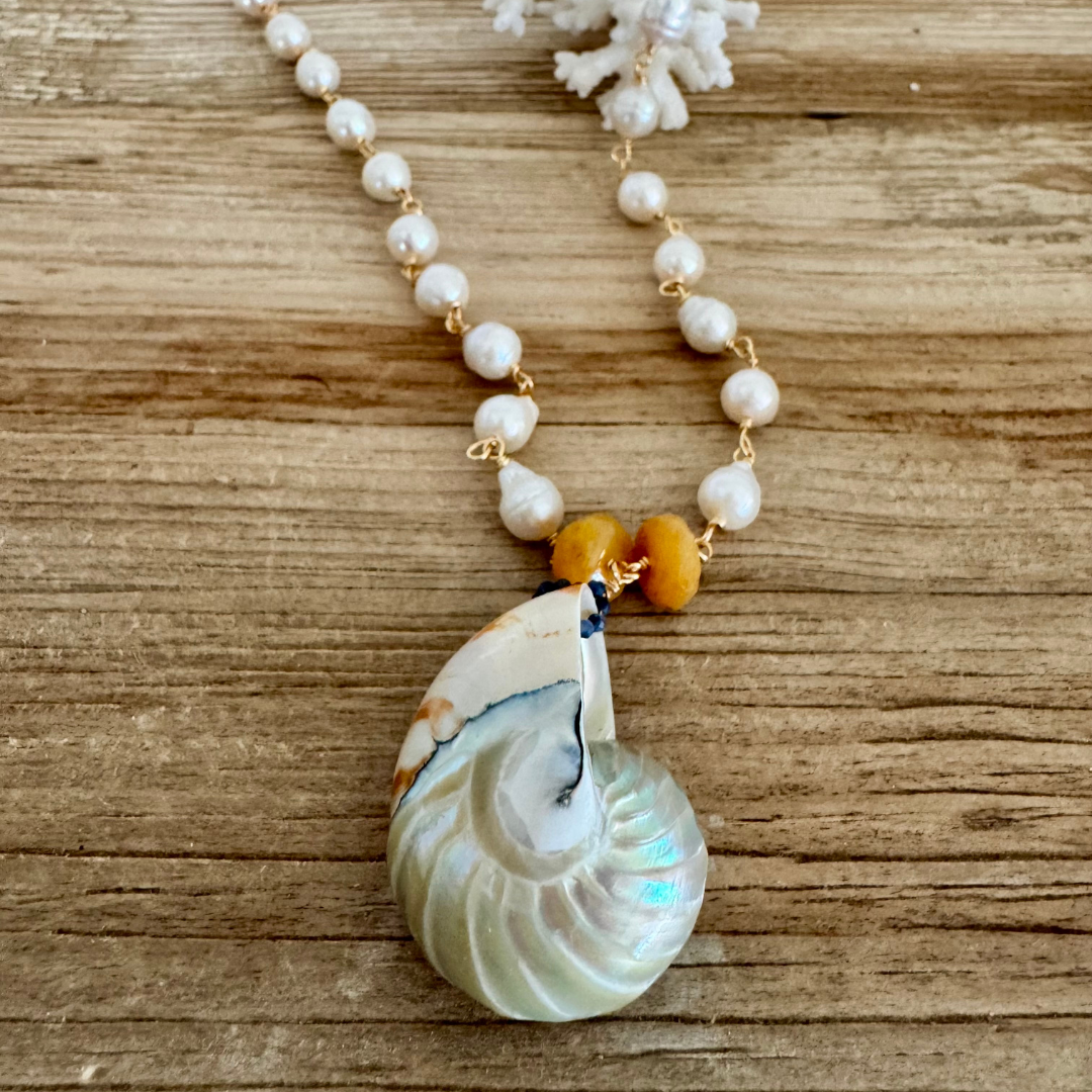 Genuine nautilus shell pendant with iridescent shimmer and hand-wrapped freshwater pearls with 14k gold filled wire, displayed against a beachy wood grain surface
Accented with yellow-orange jade gemstones for a pop of golden warmth to either side of the shell.
