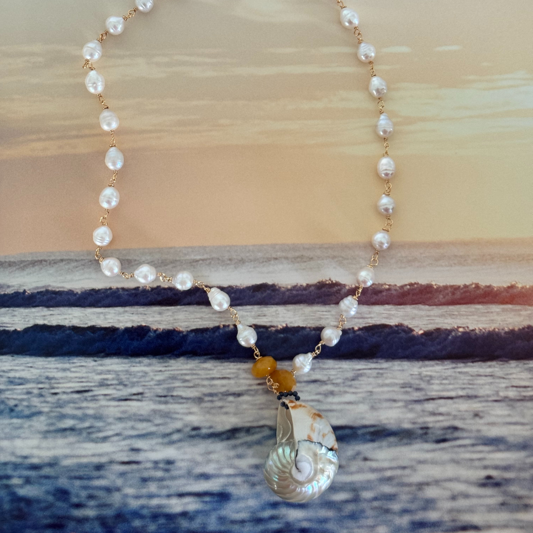 Nautilus shell pendant displayed against a magazine page showcasing navy ocean waves set against a yellow clouded sky at sunrise or sunset, displayed at aerial view.