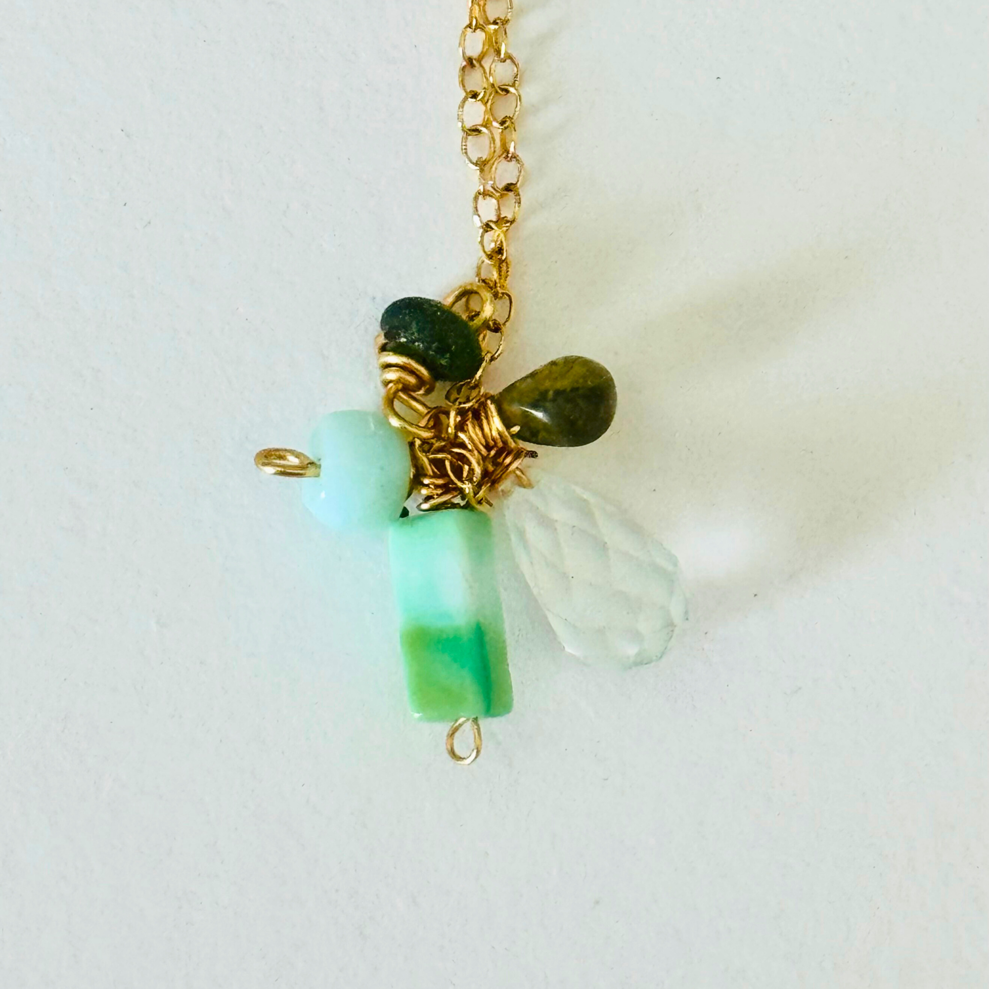 Closeup of amazonite, hessonite, and aquamarine stones at end of 14k gold filled wire chain on a white background.