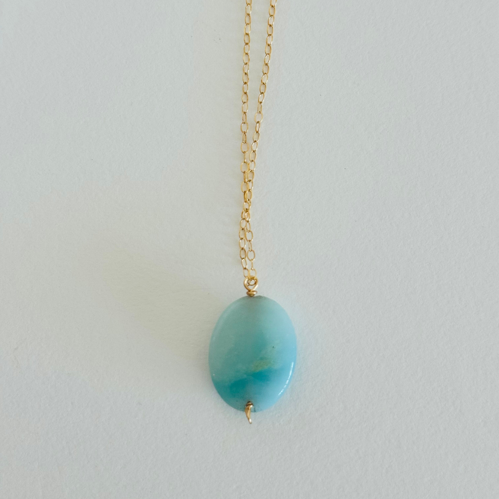 Aquamarine sea drop pendant with light blue color variation on 14k gold filled wire chain stretched vertically, laying flat.