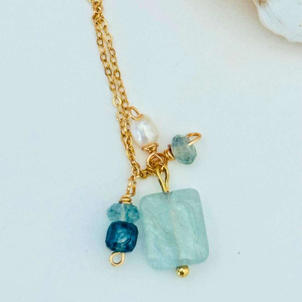 Close up view of a simple dainty 14k gold filled wire chain necklace made of aventurine, mystic blue topaz, aquamarine, and freshwater pearl stones. There are five stones total ranging from white pearl to light blue to navy blue. Displayed on a white background.