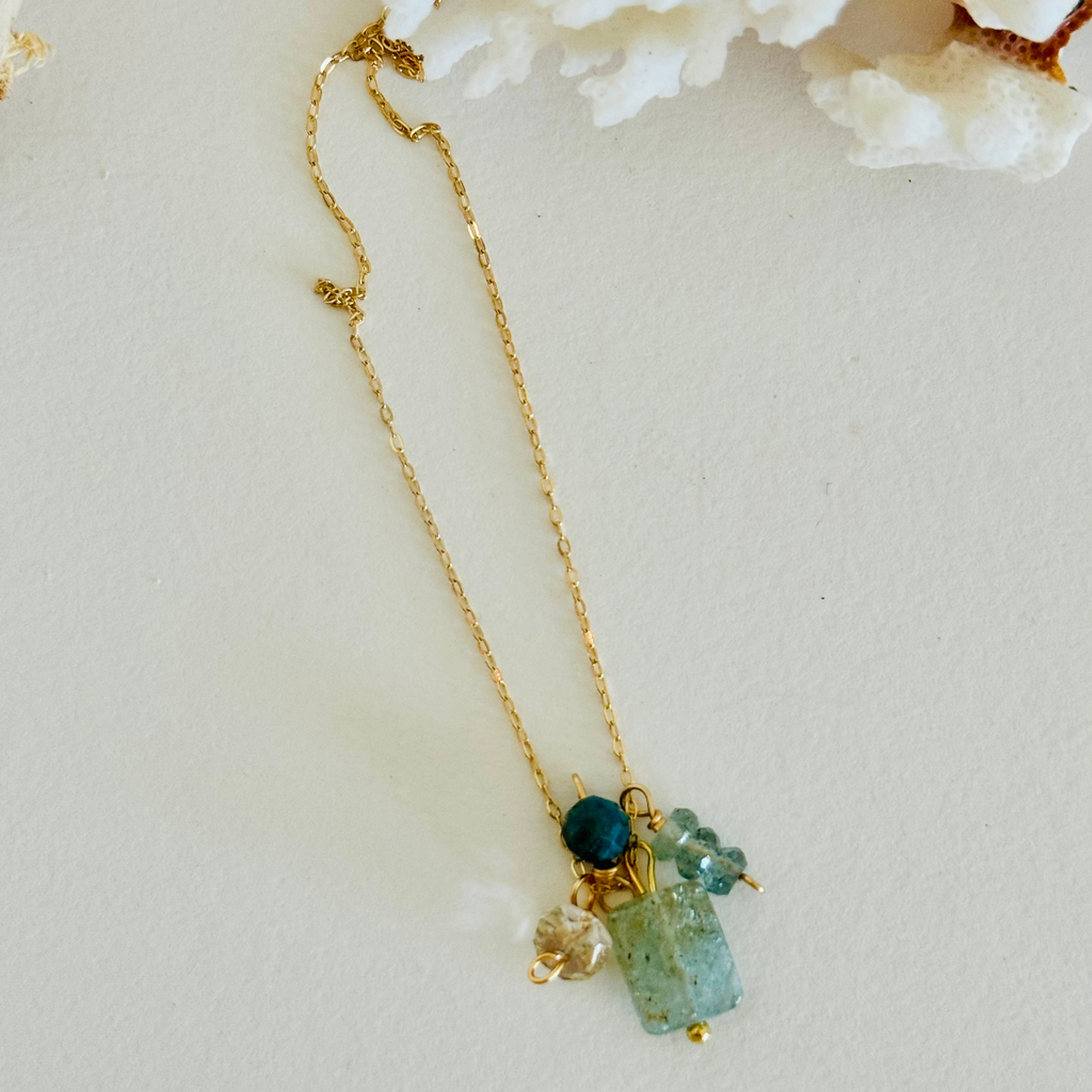 Aventurine, Apatite, Mystic Topaz, and Gold Quartz stones (one of each) on 14k gold-filled wire chain. Blue and green hues in the sones and translucent so the wiring can ever so slightly be seen through, creating contrast and warmth. Whole chain extended long, framed by white coral. On white background.