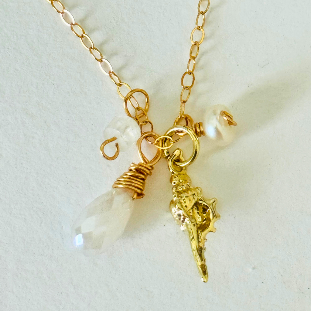 Closeup view of pearl, aquamarine, and moonstone stones and a gold seashell charm on a white background.