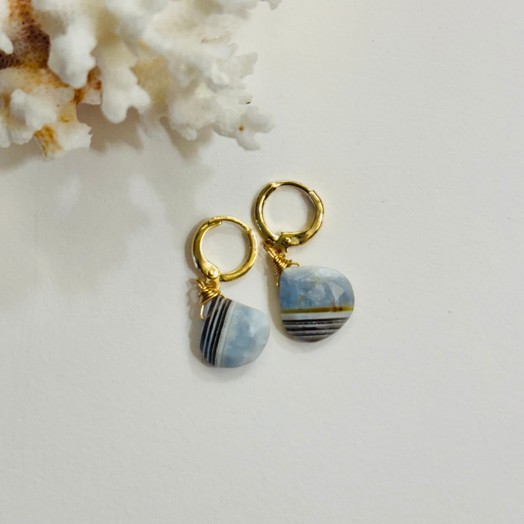 Gold hoop earrings with blue stone drops on a white background