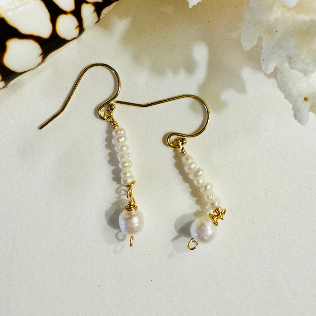 Pearl earrings with gold hooks on a textured white surface