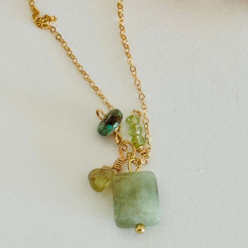 Closeup of simple gold chain with aventurine, peridot, and turquoise on white background.
