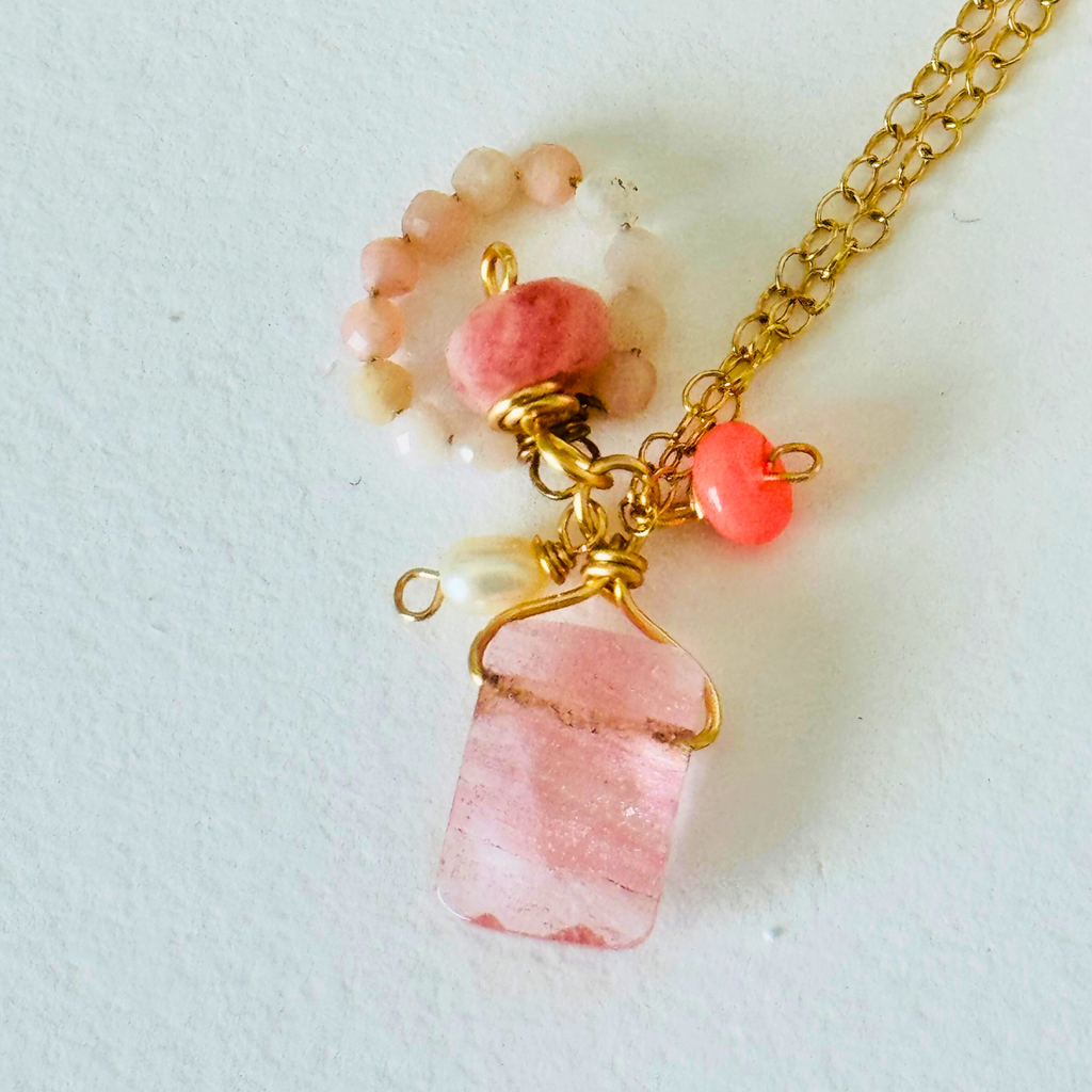 Closeup of rose quartz, pink Peruvian opal, and Ethiopian neon pink opal stones on handcrafted 14k gold filled wire chain against a white background.