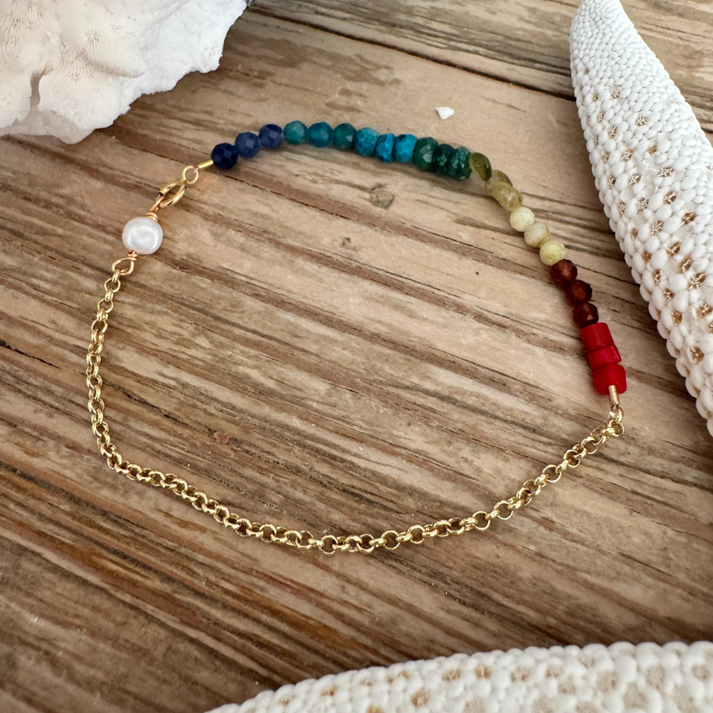 Rainbow bracelet displayed on wood surface, positioned between creamy white starfish and coral.