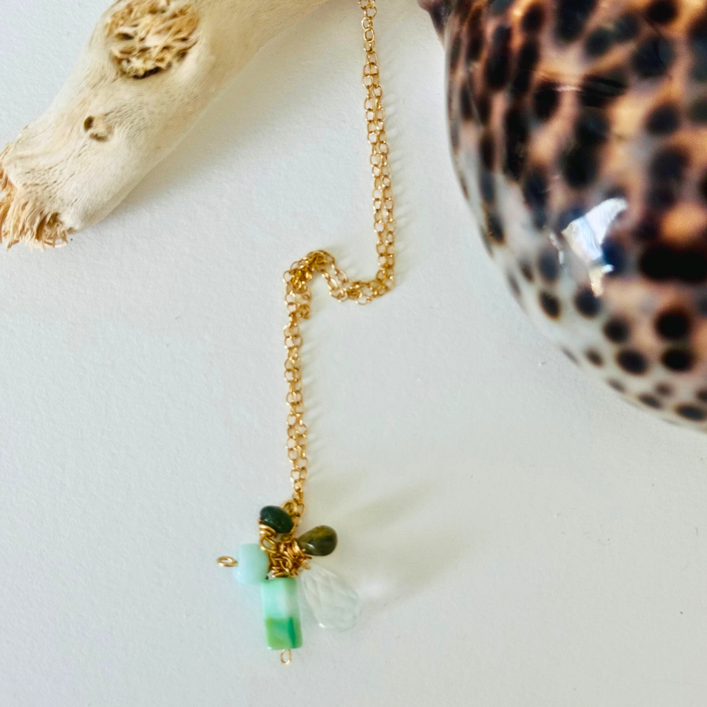 Closeup of amazonite, hessonite, and aquamarine stones at end of 14k gold filled wire chain on a white background framed by bleached driftwood and a gleaming leopard-print shell.
