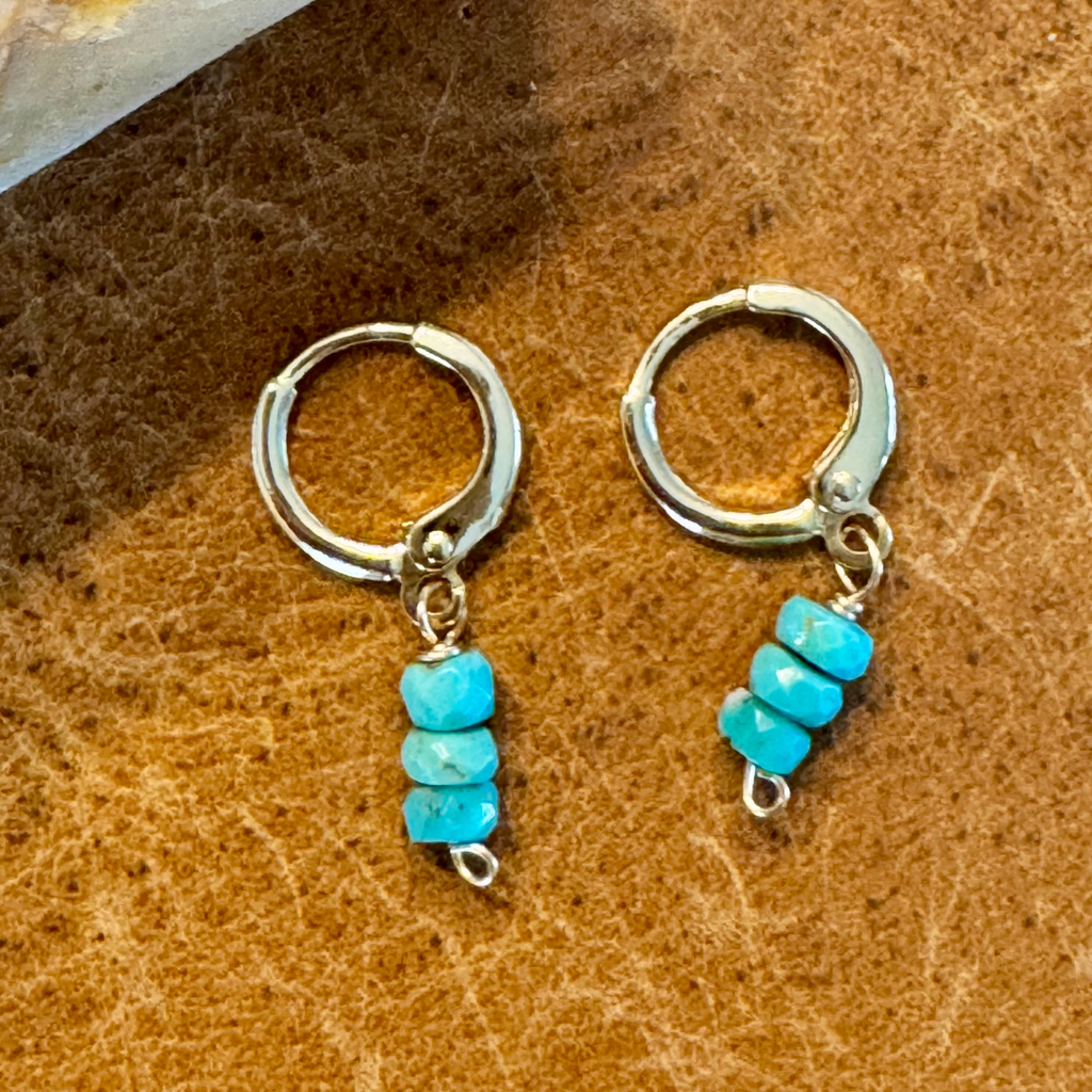 Close up view of gold-filled huggie earrings made with three wide round turquoise blue green stones stacked vertically, displayed against a warm orange yellow brown background.