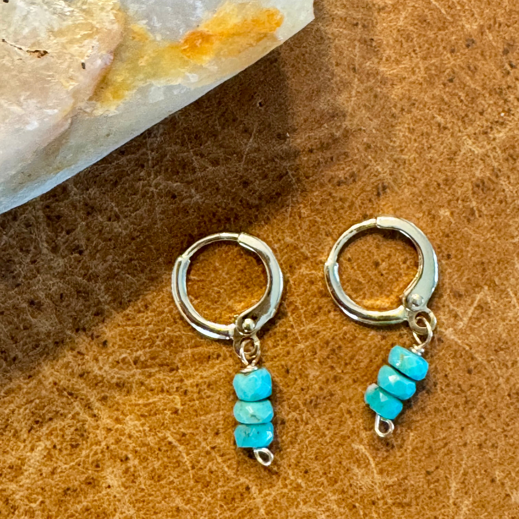 Close up view of gold-filled huggie earrings made with three wide round turquoise blue green stones stacked vertically, displayed against a warm orange yellow brown background.