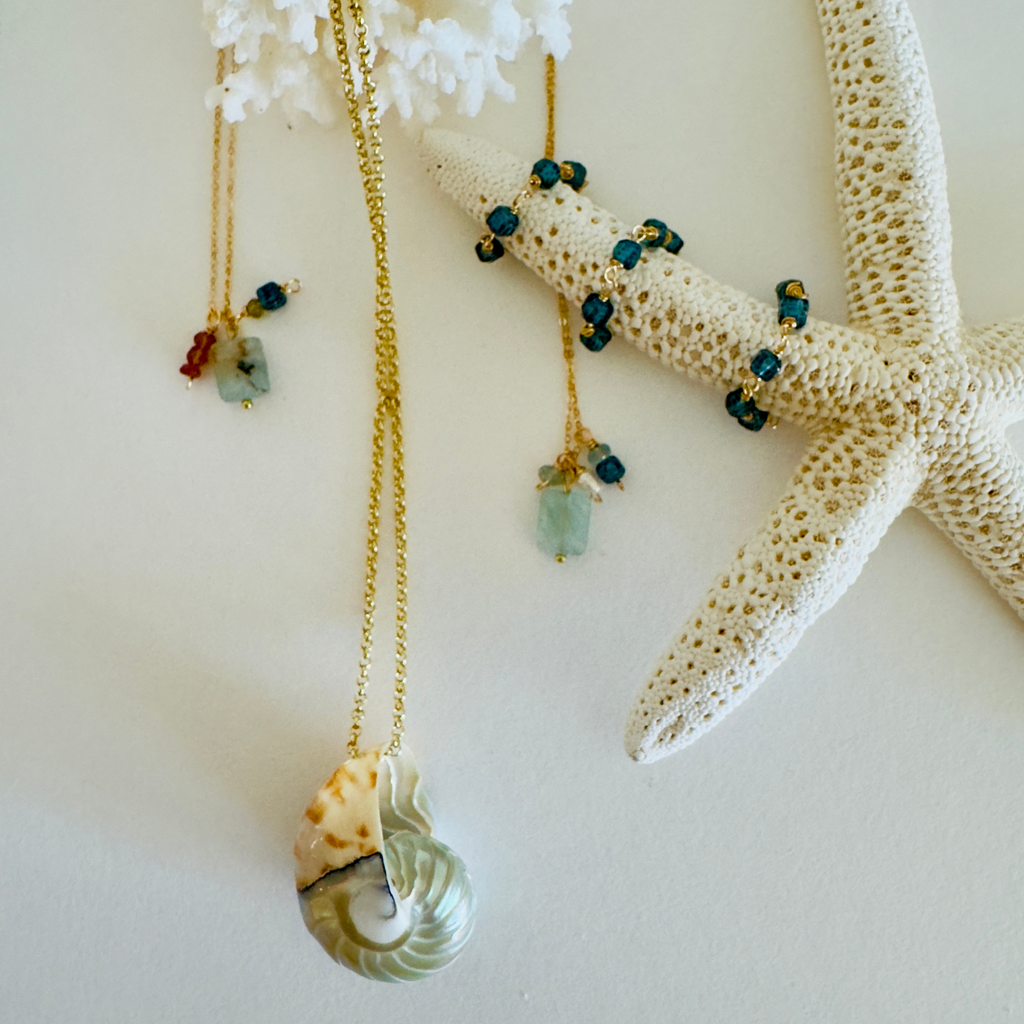 Three necklaces and three rings are displayed draped across coral and starfish on a cream white background.