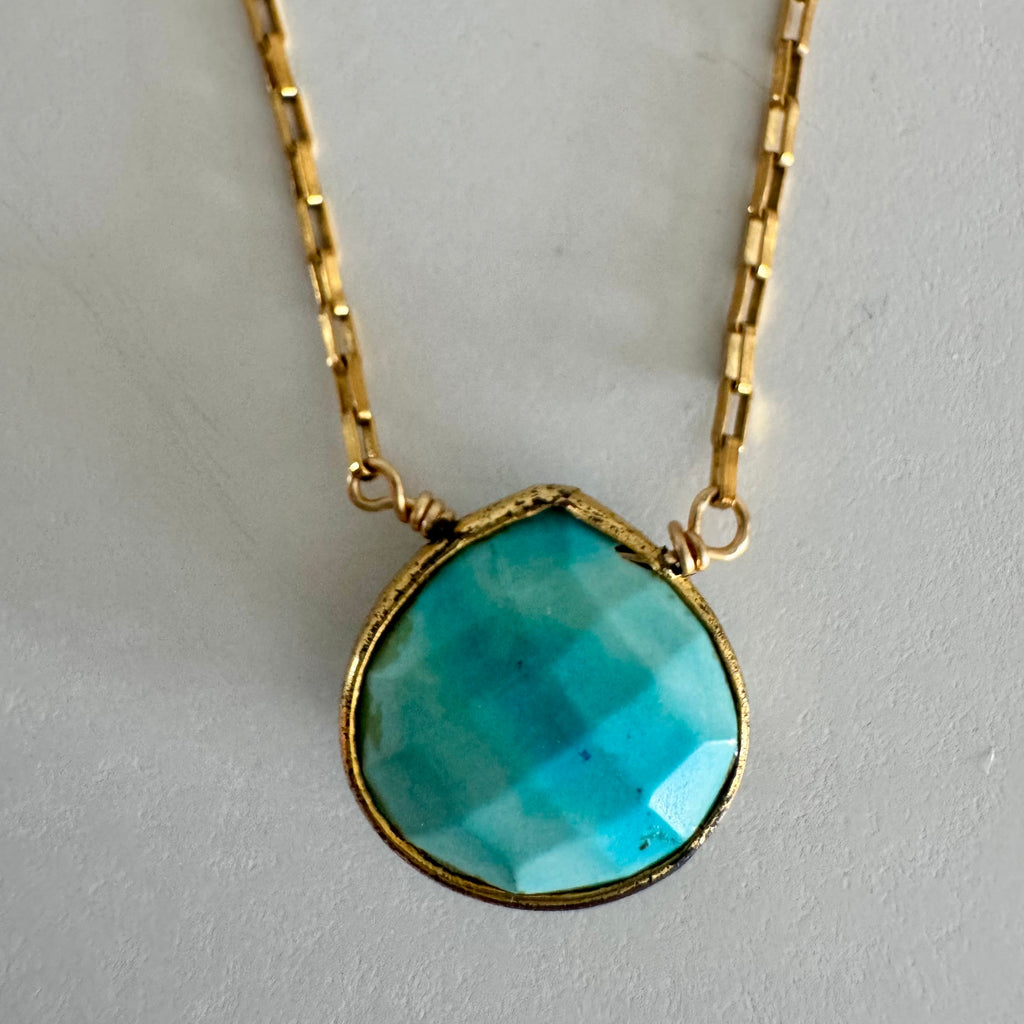 Closeup of turquoise pendant gold chain necklace on textured white background.