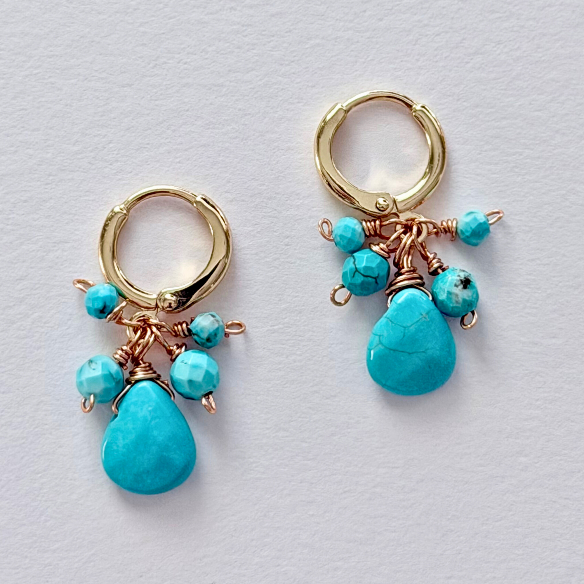 Close up of Turquoise Seas Huggie Earrings on white background. 