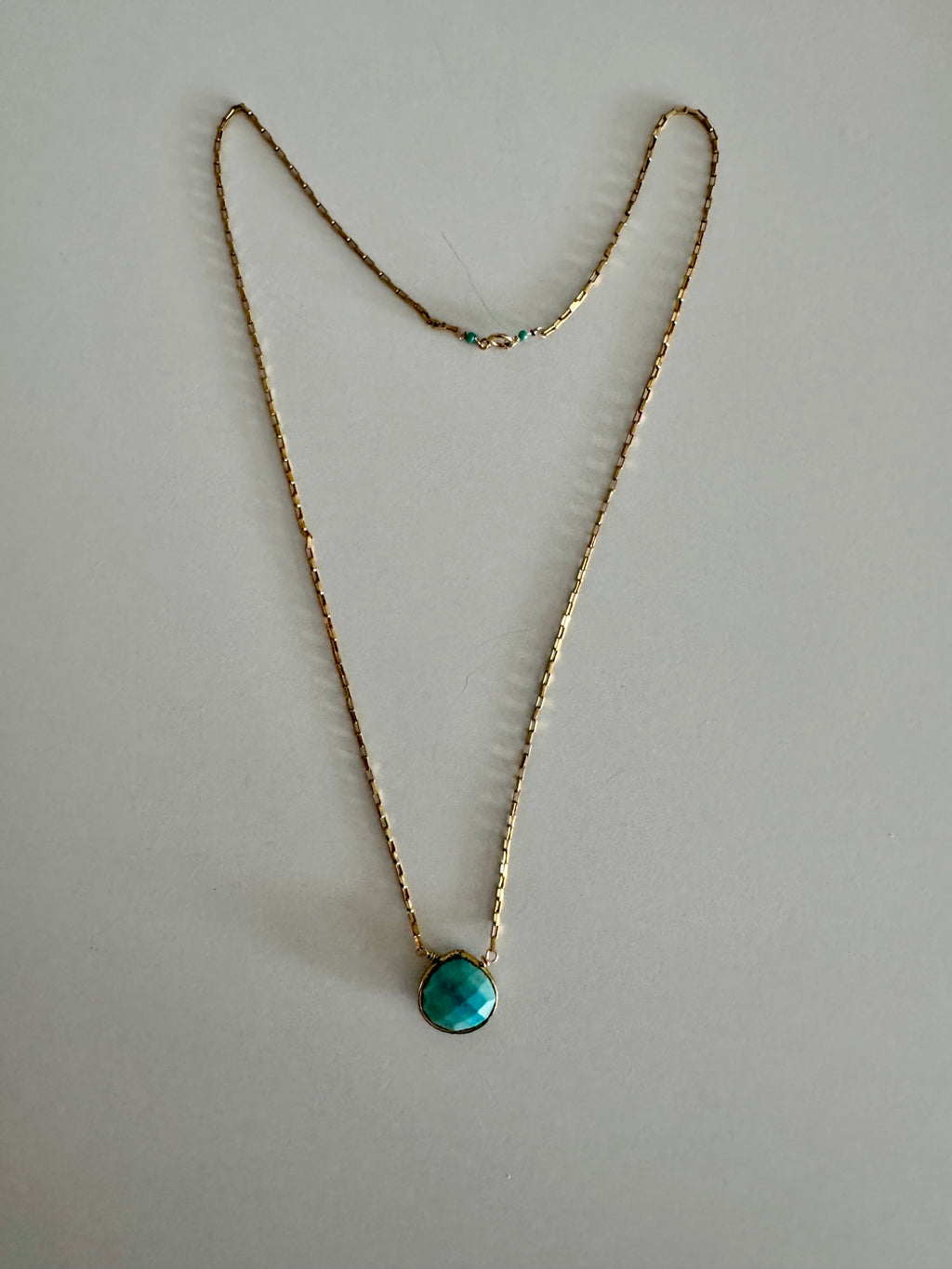 Entire turquoise pendant gold chain necklace on textured white background. Two turquoise beads offset the clasp.